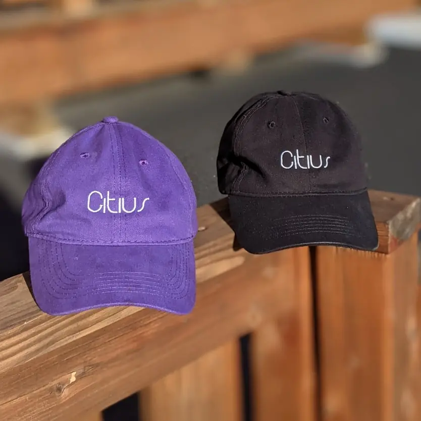 Casquettes Citius violette et noire sur une rampe en bois.